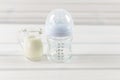 Glass baby bottle and milk jug on white wooden background