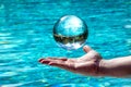 Glass ball hovers over a hand in front of water. Background with mirrored sky and trees Royalty Free Stock Photo