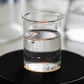 Glass beaker partly filled with clear liquid rests on a dark circular Royalty Free Stock Photo