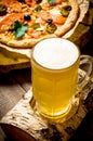 Glass of beer on birch stand and the pizza on the wooden table.