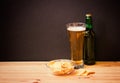 Glass of  beer, bottle of beer and potato chips on wooden table on dark background. Selective focus Royalty Free Stock Photo