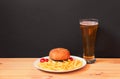 Glass of beer, burger and fried potatoes on wooden table on dark background Royalty Free Stock Photo