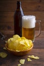 Glass of beer, potato chips in a bowl on a dark wooden background. Pouring light beer in a glass. Royalty Free Stock Photo