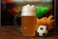 Glass with beer and snack in front of screen with football game. Soccer fans