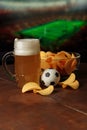 Glass of beer, soccer ball and snack in front of screen with football game. Vertical image Royalty Free Stock Photo