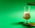 A glass of beer stands on a green background and a jet of beer from a green bottle. Nearby are chips and clover leaves Royalty Free Stock Photo