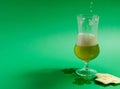 A glass of beer stands on a green background and a jet of beer from a green bottle. Nearby are chips and clover leaves Royalty Free Stock Photo