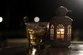 A glass of beer and white lantern with candle light inside on the table.