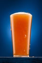 a glass of beer on a wooden stand and a dark blue background, pouring beer into a glass, a close view of the object, the beer Royalty Free Stock Photo