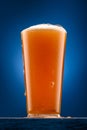 a glass of beer on a wooden stand and a dark blue background, pouring beer into a glass, a close view of the object, the beer Royalty Free Stock Photo
