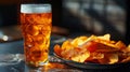 A glass of beer is on a wooden table next to a plate of chips Royalty Free Stock Photo