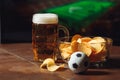 A glass of beer on a wooden table with potato chips. Football on a background Royalty Free Stock Photo