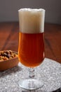 Glass of Belgian light blond beer made in abbey and bowl with party mix nuts Royalty Free Stock Photo