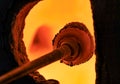 Glass blower working on a bubble of melted glass on a rod by heating it up in a kiln at a glass maker& x27;s workshop