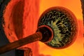 Glass blower working on a bubble of melted glass on a rod by heating it up in a kiln at a glass maker& x27;s workshop