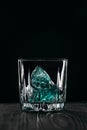 Glass with blue ice cubes. Pouring gin into a glass on a wooden table. Gin in a glass on a black background Royalty Free Stock Photo