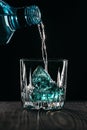 Glass with blue ice cubes. Pouring gin into a glass on a wooden table. Gin in a glass on a black background Royalty Free Stock Photo