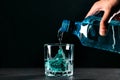 Glass with blue ice cubes. Pouring gin into a glass on a wooden table. Gin in a glass on a black background Royalty Free Stock Photo