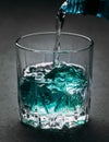 Glass with blue ice cubes. Pouring gin into a glass on a wooden table. Gin in a glass on a black background Royalty Free Stock Photo