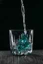 Glass with blue ice cubes. Pouring gin into a glass on a wooden table. Gin in a glass on a black background Royalty Free Stock Photo