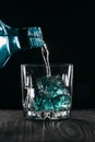 Glass with blue ice cubes. Pouring gin into a glass on a wooden table. Gin in a glass on a black background Royalty Free Stock Photo