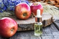 Glass bottle of apple essential oil near fresh apples on a wooden table. Essential oil is used to fill lamps, perfumes and in