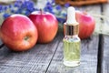 Glass bottle of apple essential oil near fresh apples on a wooden table. Essential oil is used to fill lamps, perfumes and in