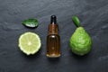 Glass bottle of bergamot essential oil and fresh fruits on black slate table, flat lay Royalty Free Stock Photo