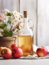 Glass bottle with cider vinegar and ripe apples on light wooden background, close-up, Provence style, vertical image.