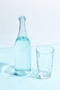 A glass bottle with clear water and a glass on a white-blue background. Minimalistic creative concept Royalty Free Stock Photo