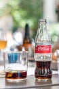 A glass bottle of Coca Cola light taste on a table outdoors.