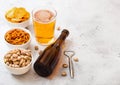 Glass and bottle of craft lager beer with snack and opener on stone kitchen table background. Pretzel and crisps and pistachio in Royalty Free Stock Photo