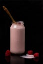 A glass bottle of crimson yogurt with a wooden spoon and raspberry berries