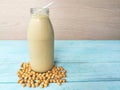 A glass bottle soy milk, soybeans seed around base, blue wooden table,