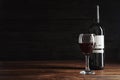 Glass and bottle with delicious red wine on wooden table against dark background Royalty Free Stock Photo