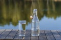 Glass and bottle with drinking water on a wooden table in the morning near the lake. Nature and travel concept Royalty Free Stock Photo