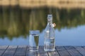 Glass and bottle with drinking water on a wooden table in the morning near the lake. Nature and travel concept Royalty Free Stock Photo