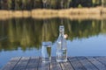 Glass and bottle with drinking water on a wooden table in the morning near the lake. Nature and travel concept Royalty Free Stock Photo
