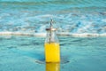 Glass bottle with fresh tropical fruits juice with straw standing on beach sand shore blue turquoise foamy sea waves Royalty Free Stock Photo