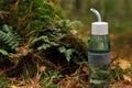 Glass bottle of fresh water on ground in forest, space for text Royalty Free Stock Photo