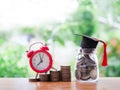 Glass bottle with graduation hat and red alarm on stack of coins. The concept of saving money for education, student loan, Royalty Free Stock Photo