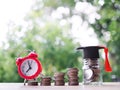 Glass bottle with graduation hat and red alarm on stack of coins. The concept of saving money for education, student loan, Royalty Free Stock Photo