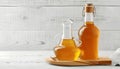 Glass bottle and gravy boat with fresh apple cider vinegar on white wooden background