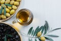 Glass bottle of homemade olive oil and olive tree branch, raw turkish green and black olive seeds and leaves on white table Royalty Free Stock Photo