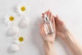 Glass bottle with moisturizing serum in female hands with white manicure.