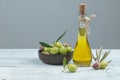 Glass bottle of olive oil and wooden breakfast bowl with raw turkish olive seeds and leaf on white rustic vintage table. Olives b Royalty Free Stock Photo