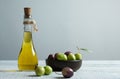 Glass bottle of olive oil and wooden breakfast bowl with raw turkish olive seeds and leaf on white rustic vintage table. Olives b Royalty Free Stock Photo