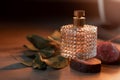 Glass bottle of perfume on stones with branches of greenery on wooden background. Natural fresh scent for men or women