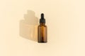 A glass bottle with a pipette for essential oil, lotion or serum on a pastel beige background. Dark amber glass bottle