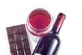 A glass, a bottle of red wine, a bar of chocolate on a white background.